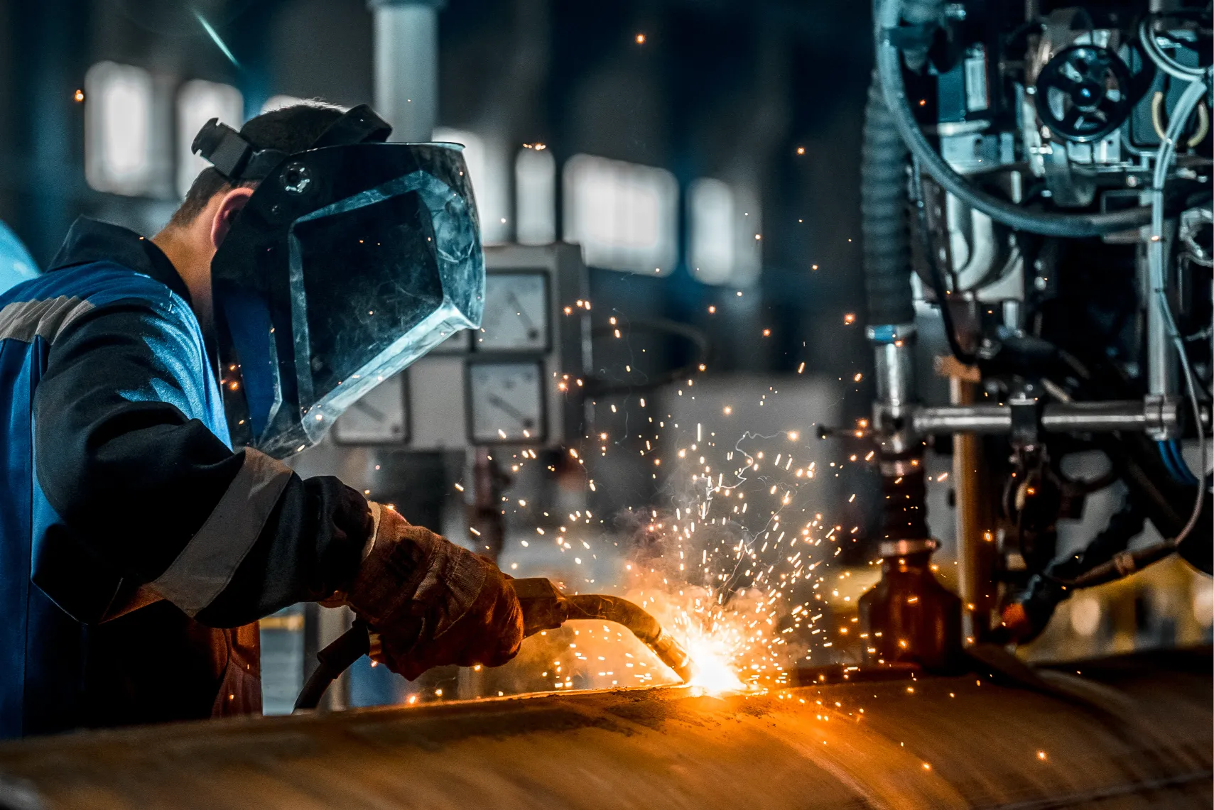 A worker in protective gear uses a welding torch purchased with Borrow Bridge Cash flow funding. Shows a metal pipe, producing bright sparks in an industrial setting