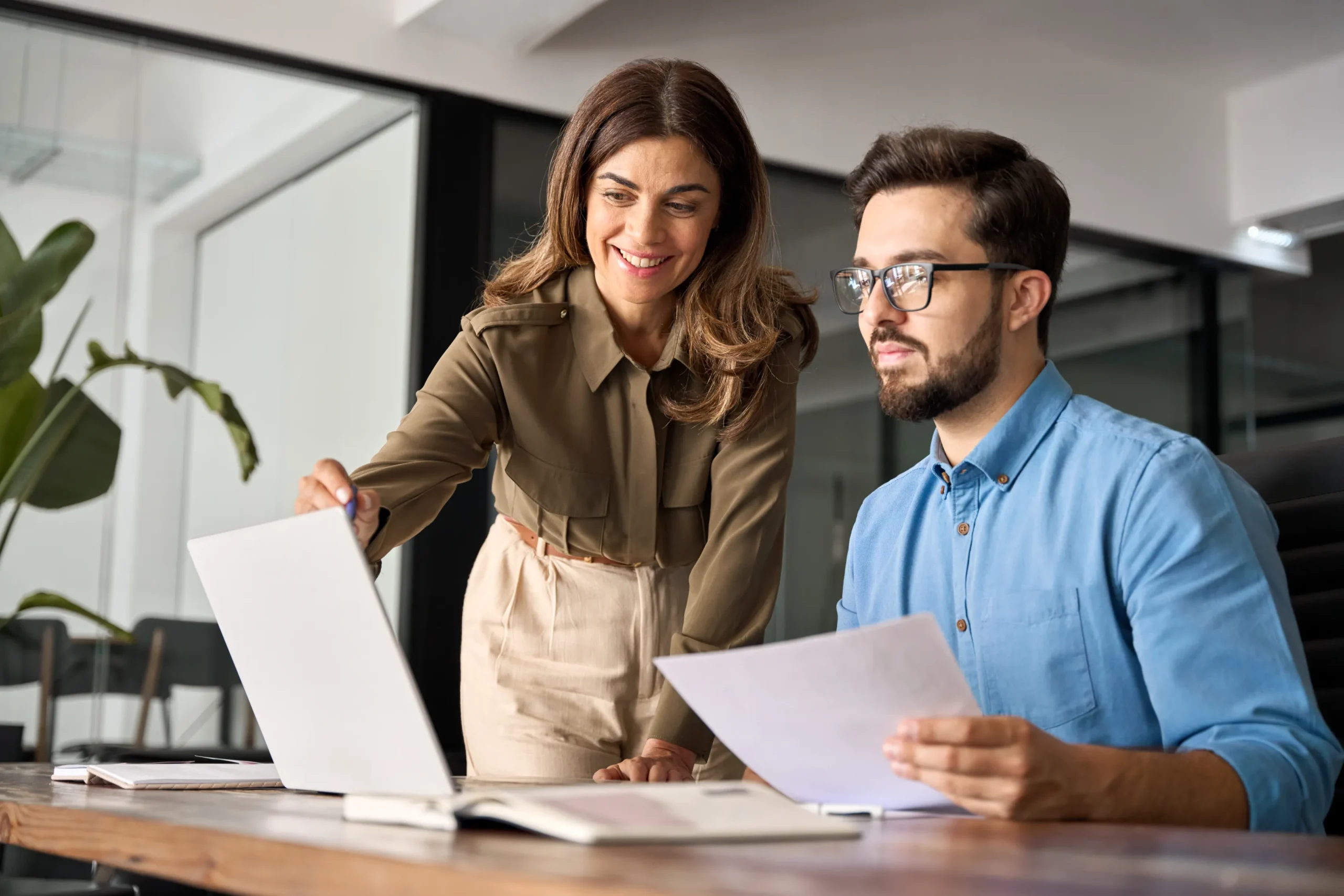 A woman stands and points at a laptop screen while a seated man holds papers, they are talking about fast and affordable personal loan options.