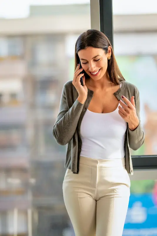 A woman stands indoors by a window, smiling and talking on her mobile phone to Harrison from Borrow Bridge about a flexible personal loan