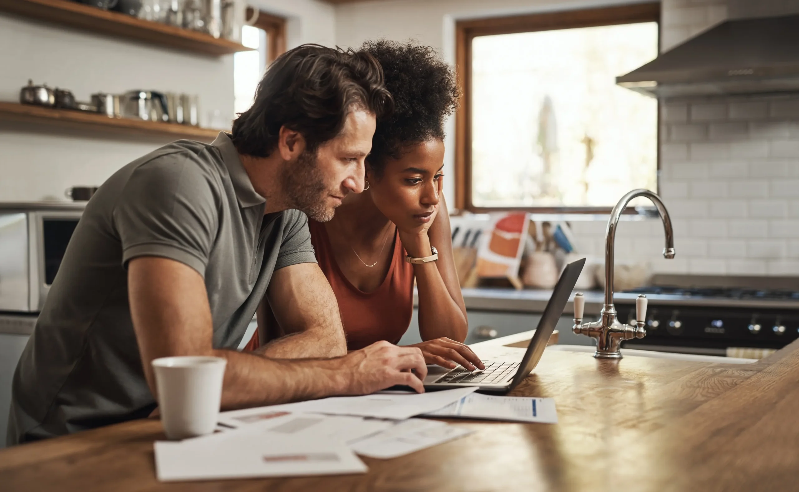 A man and woman sit at a kitchen worktop looking at a laptop, using the Personal Loan Calculator from Borrow Bridge.